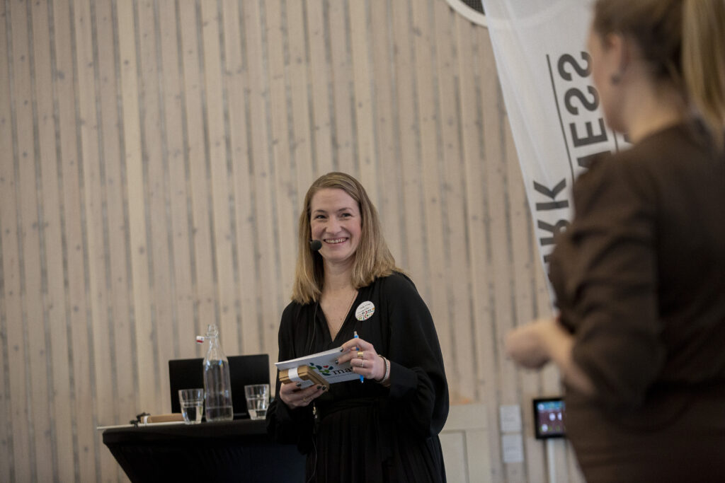 En leende kvinna håller i manuskort och intervjuar annan kvinna.